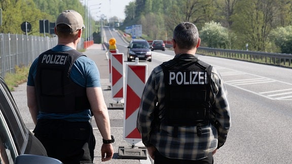 Zwei Polizisten der Gemeinsamen Fahndungsgruppe (GFG) der Bundes- und Landespolizei stehen am Grenzübergang der deutsch-polnischen Grenze am Straßenrand und beobachten den Verkehr.