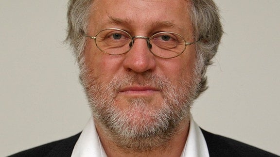 Poträt-Bild grauhaariger, graubärtiger Mann mit Brille in weißem Hemd und Jackett